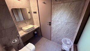 A bathroom with a sink, mirror, toilet, and shower area. - Hotel Kushala Grand, Dombivali (Ambernath)
