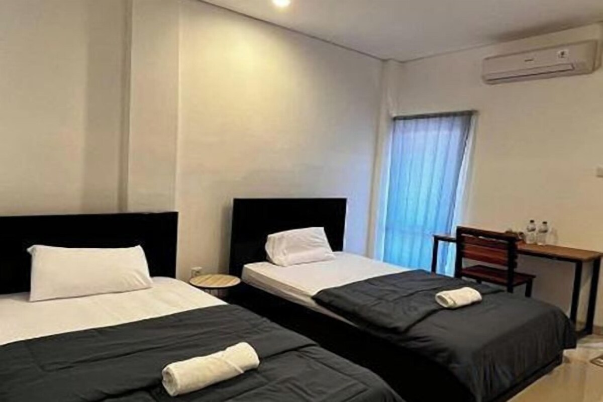 Une chambre d’hôtel avec deux lits, un bureau et une fenêtre avec des rideaux.