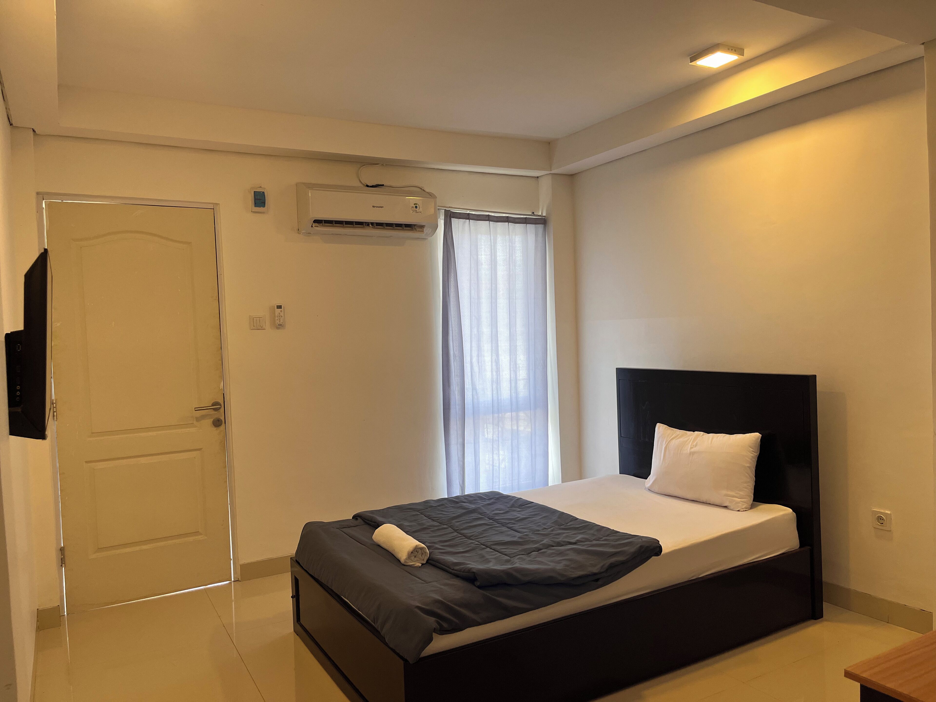Une chambre à coucher avec un lit, une porte, un appareil de climatisation et une fenêtre avec des rideaux.