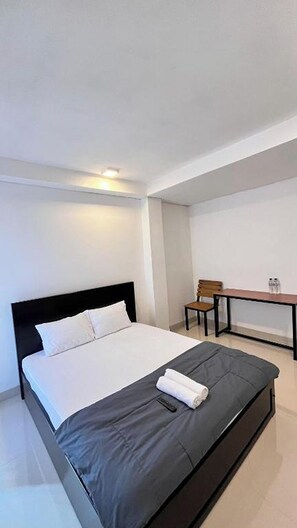 A modern hotel room with a large bed, a small table, and a chair. - Bluebell House (Labuan Bajo)