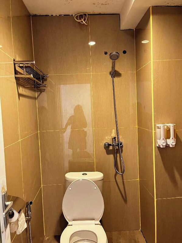 A small, tiled bathroom with a toilet, a shower, and a towel rack.