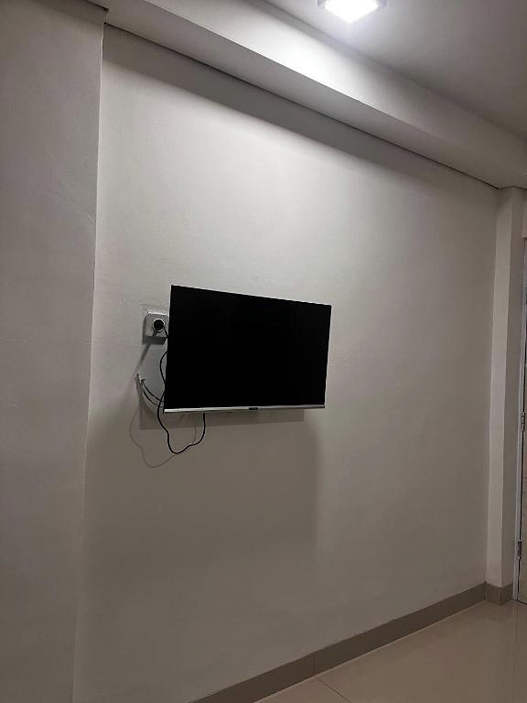 Une pièce dotée d’un téléviseur à écran plat fixé au mur, d’une prise de courant et d’une porte située sur le côté droit.