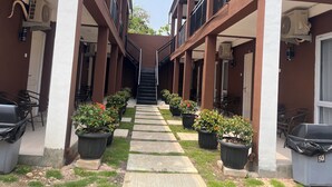 A corridor with potted plants, outdoor seating, and air conditioning units.