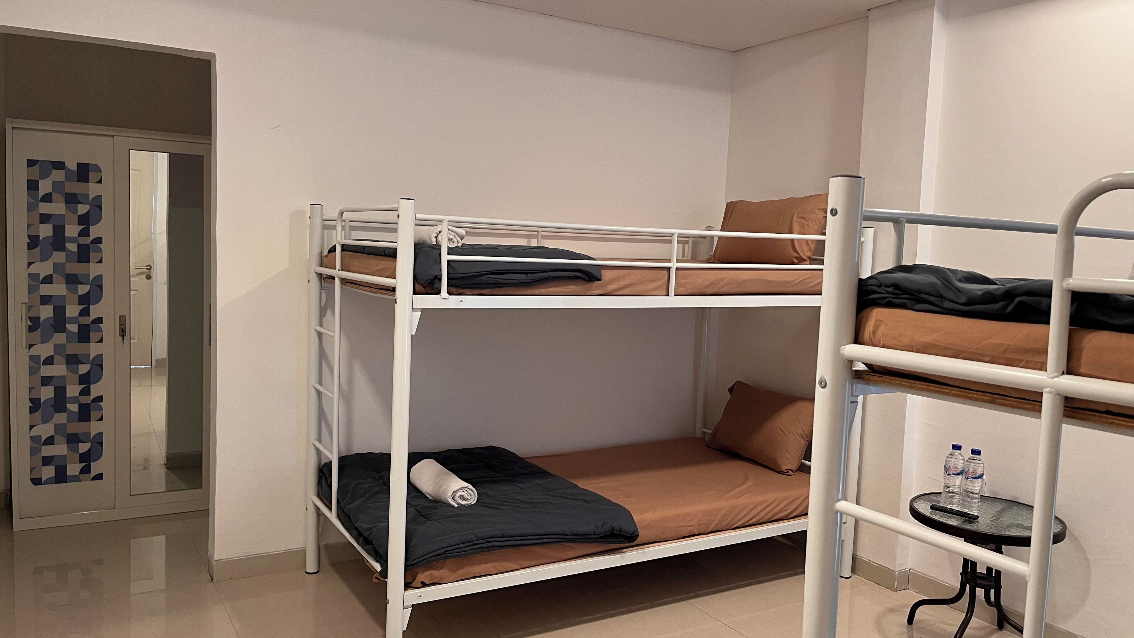 Habitación con literas, una puerta y una mesita con botellas de agua.