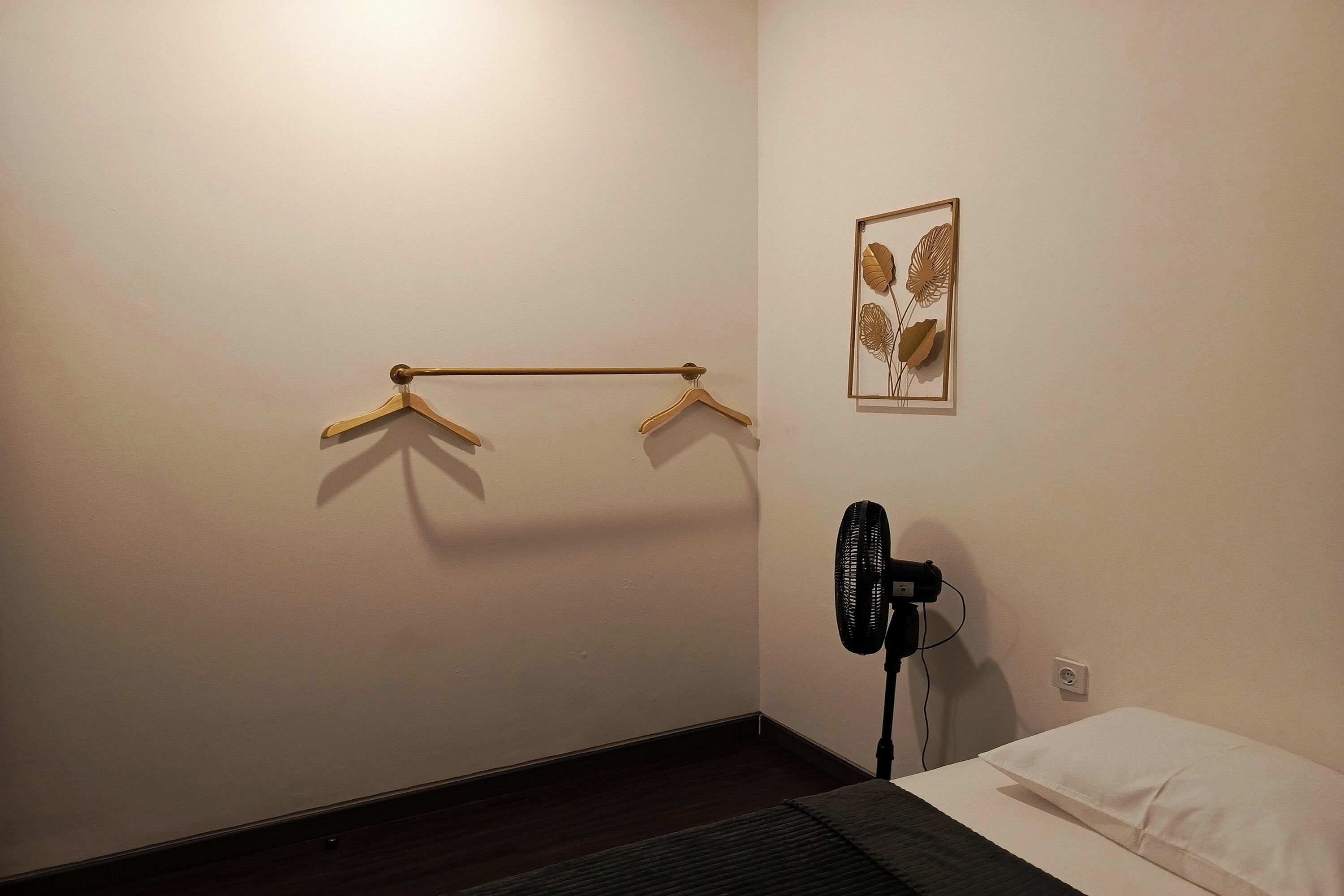 Un dormitorio con cama, un ventilador de pie y un perchero en la pared.
