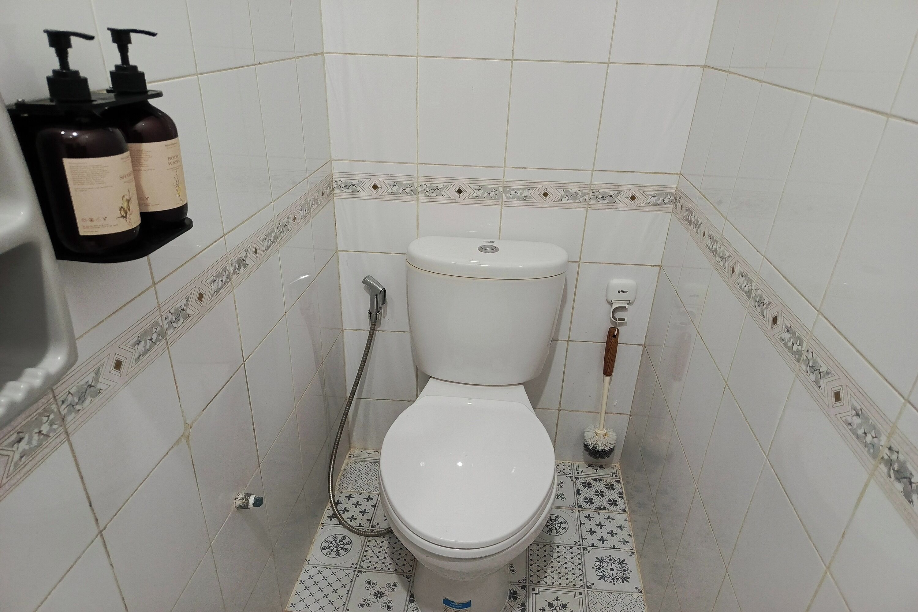 Un bagno piccolo con il water, un asciugatore di mani e due flaconi di shampoo su uno scaffale.