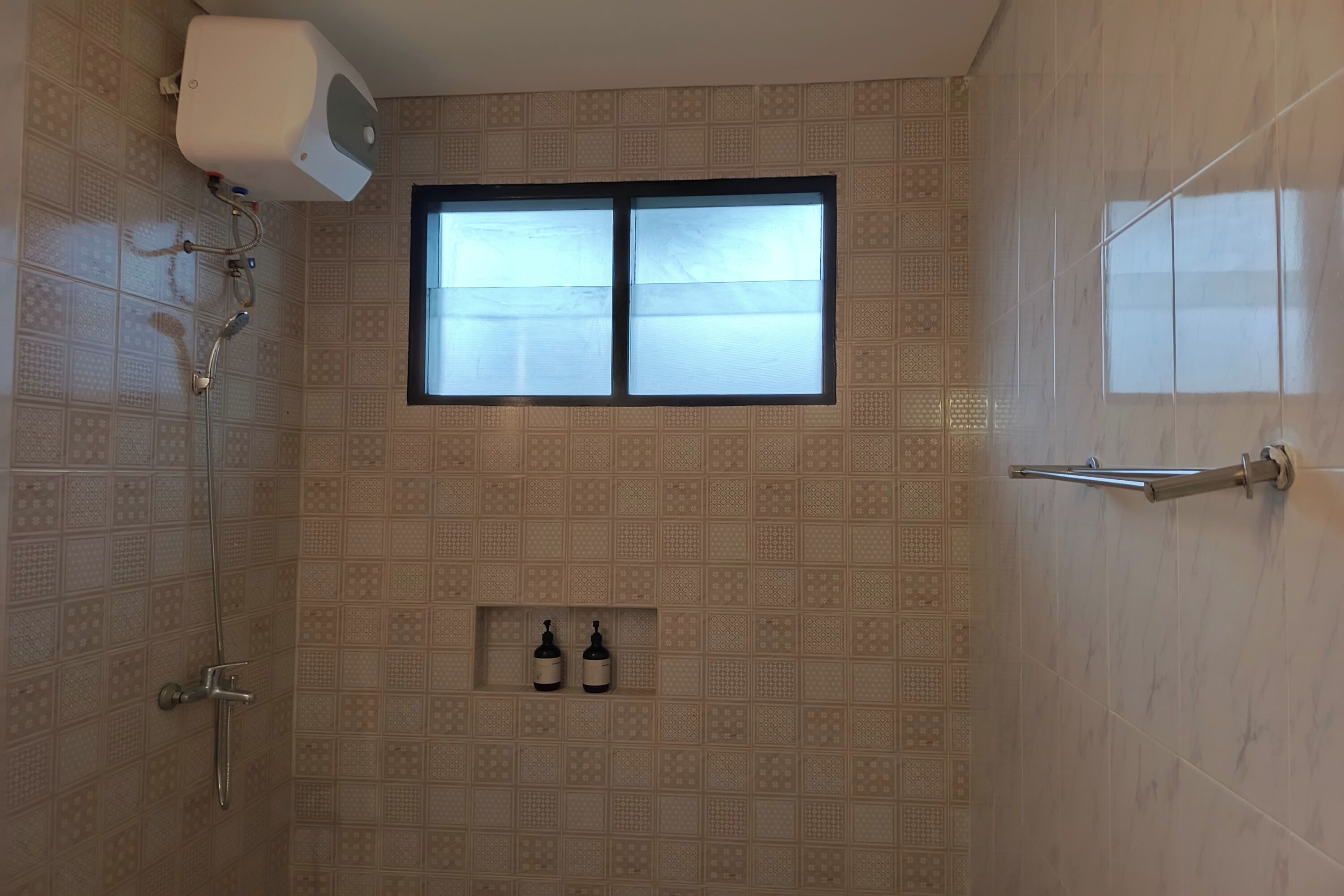 Una ducha con ventana, un perchero y dos botellas en la pared.