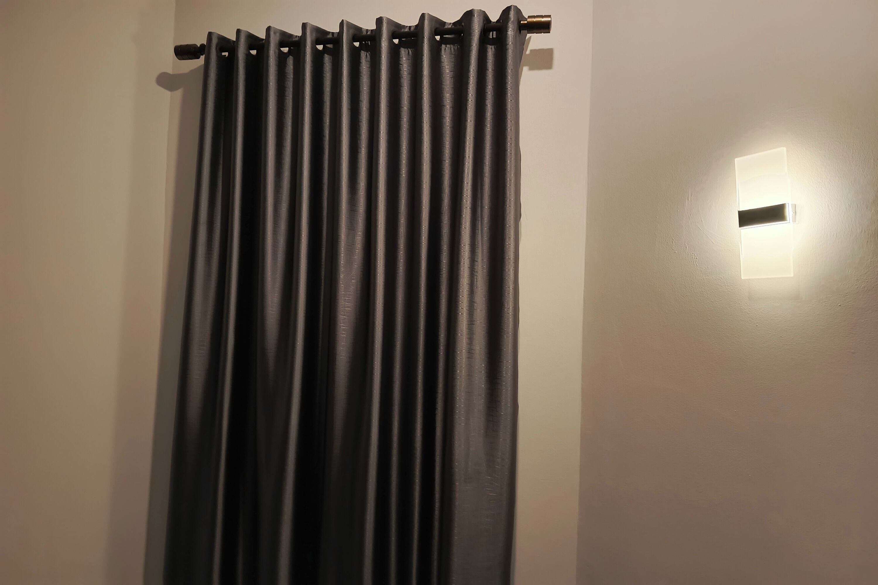 Una habitación con cortina negra, una lámpara de pared y un picaporte a la vista.