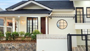 A two-story house with a tiled roof, a stone foundation, and a small garden with shrubs.