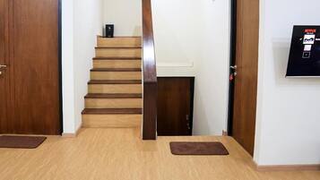 A room with a wooden staircase, a flat-screen TV mounted on the wall, and two brown mats on the floor.