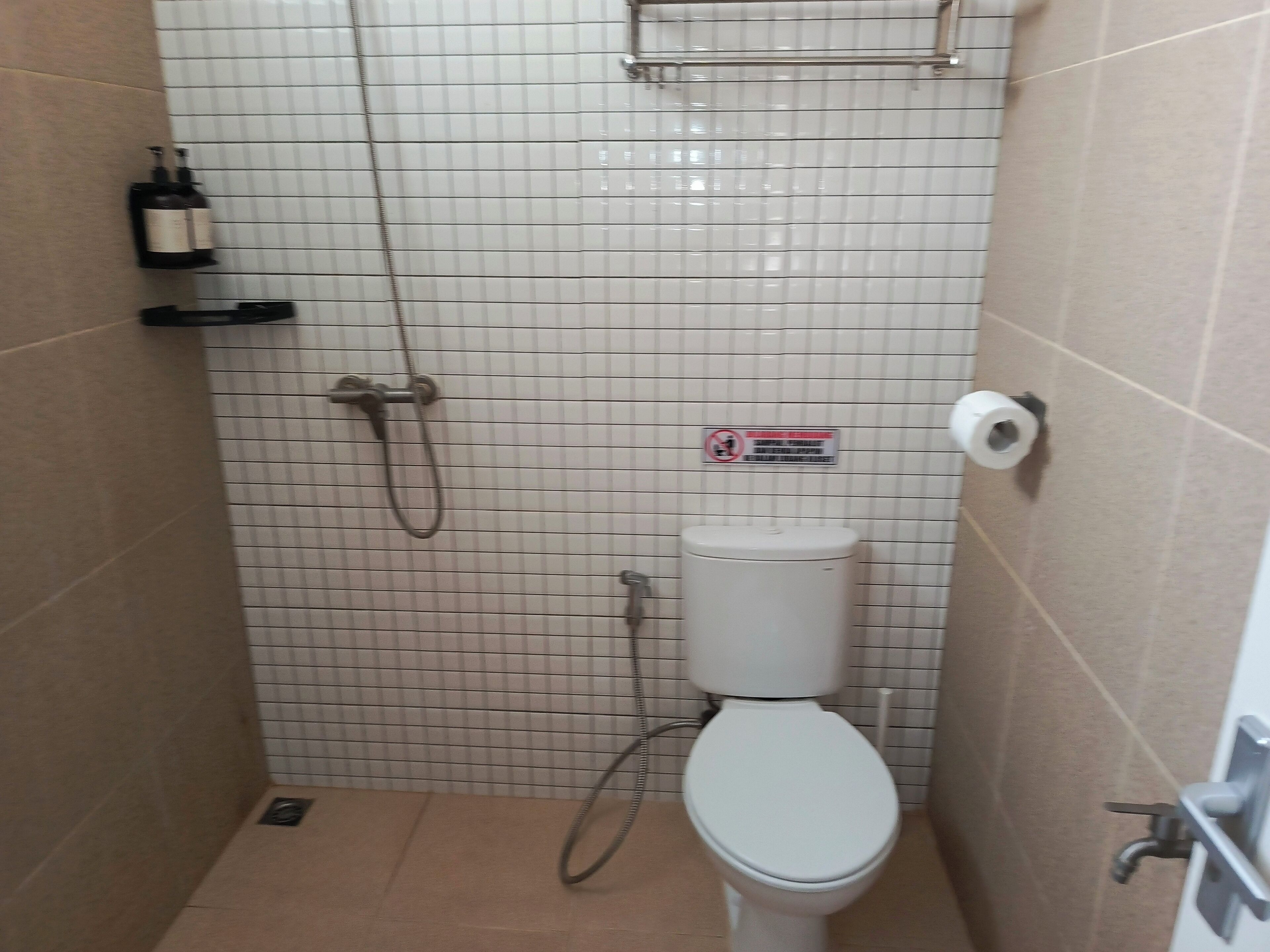 A small, tiled bathroom with a toilet, a shower, and a shelf with a bottle.