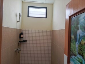 Una ducha con cabezal de ducha manual, una ventana arriba y pared de azulejos.