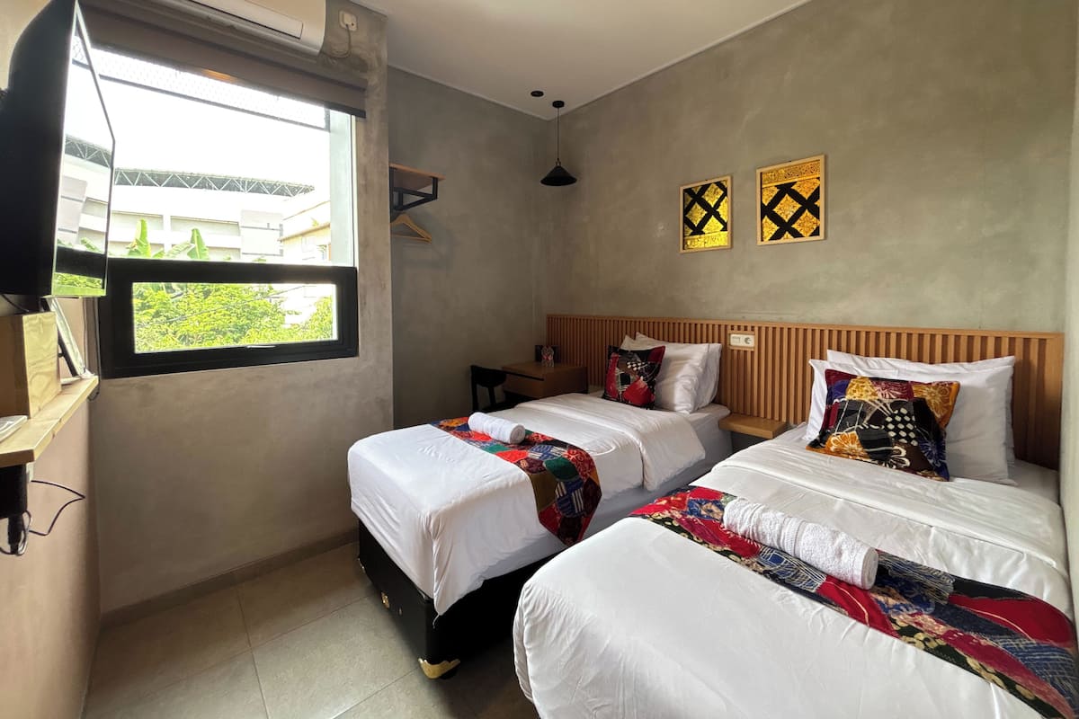 Quarto de hotel com duas camas, janela com vista, TV na parede e ventoinha no teto.