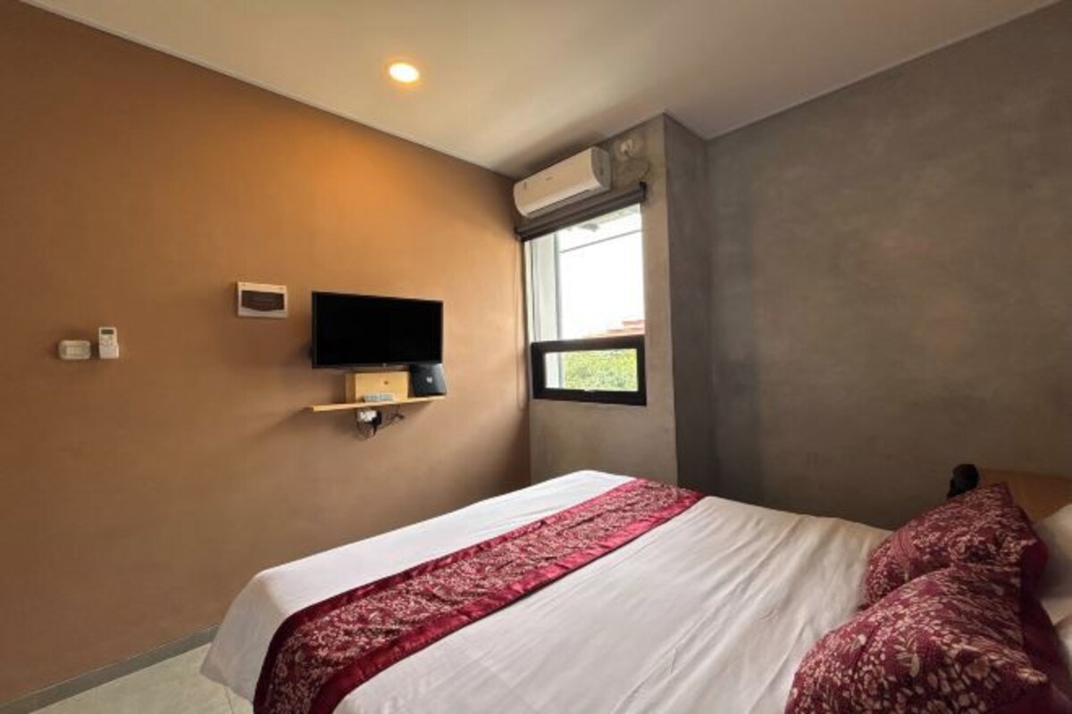 A hotel room with a bed, a television mounted on the wall, and an air conditioning unit.