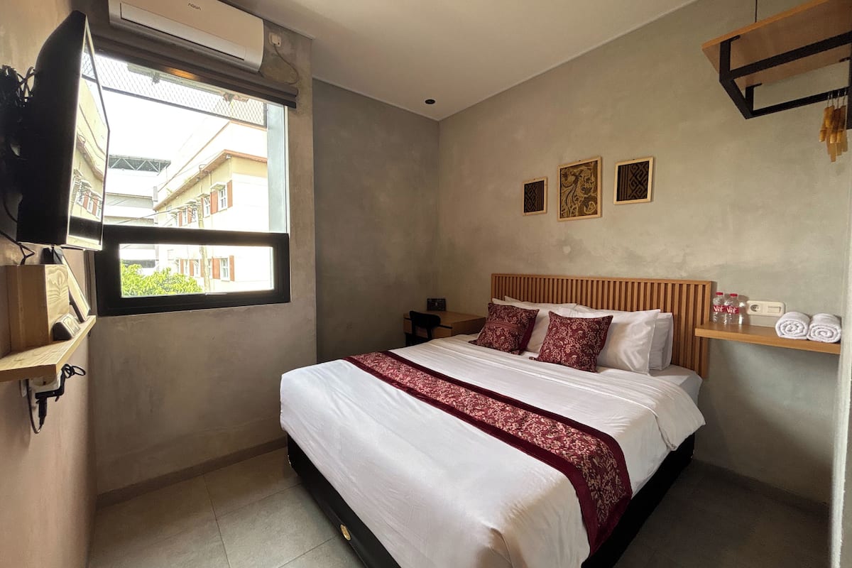 Quarto com cama, televisão na parede, janela e prateleira com toalhas.