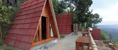 A bungalow with a sloped red roof, wooden exterior, and a concrete patio.