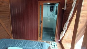 Een houten kamer met een bed, een douchegedeelte en een deur die leidt naar een trap.