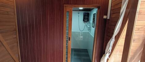 Una habitación tipo cabaña de madera, con cama, zona de ducha y puerta que da a una escalera.