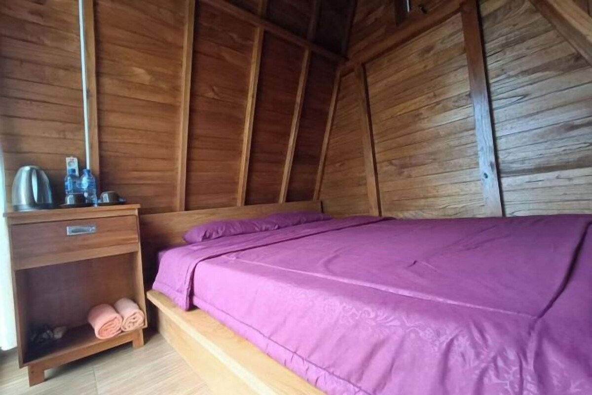 Een houten kamer met een bed, nachtkastje en een plank met handdoeken.