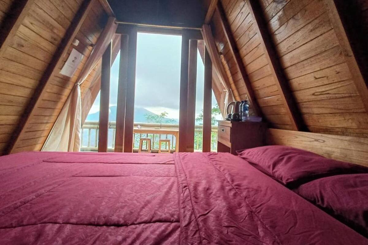 Een kamer met houten wanden en een hoog plafond, met een bed en uitzicht op bergen.