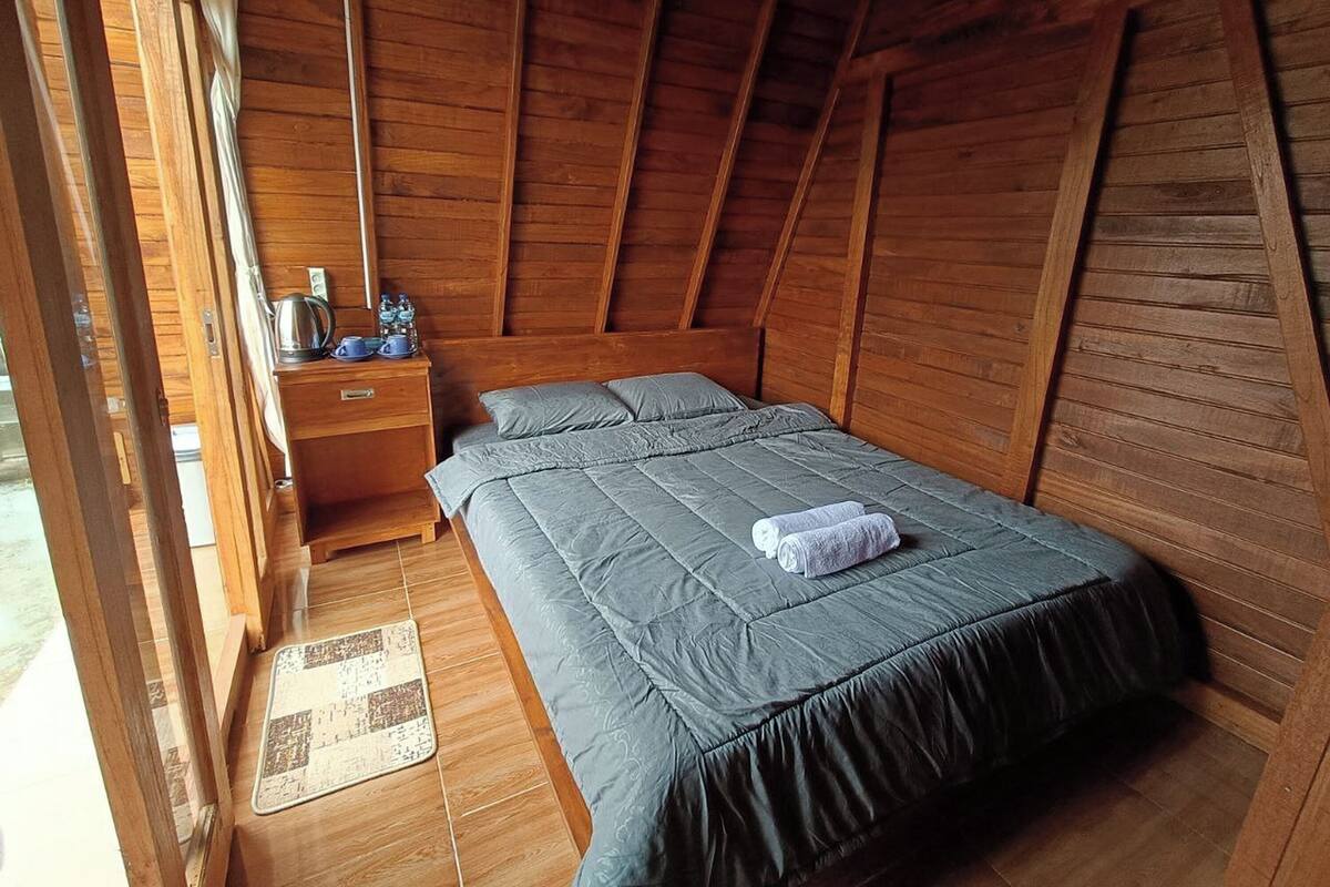 Een houten kamer met een bed, een nachtkastje en een kleine tafel met waterkoker en kopjes.