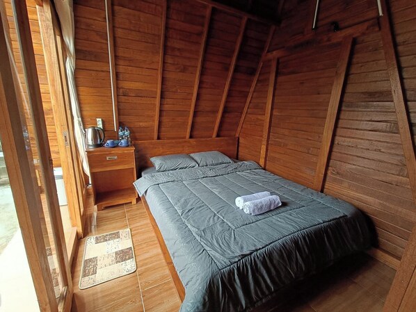 A wooden room with a bed, a nightstand, and a small table with a kettle and cups.