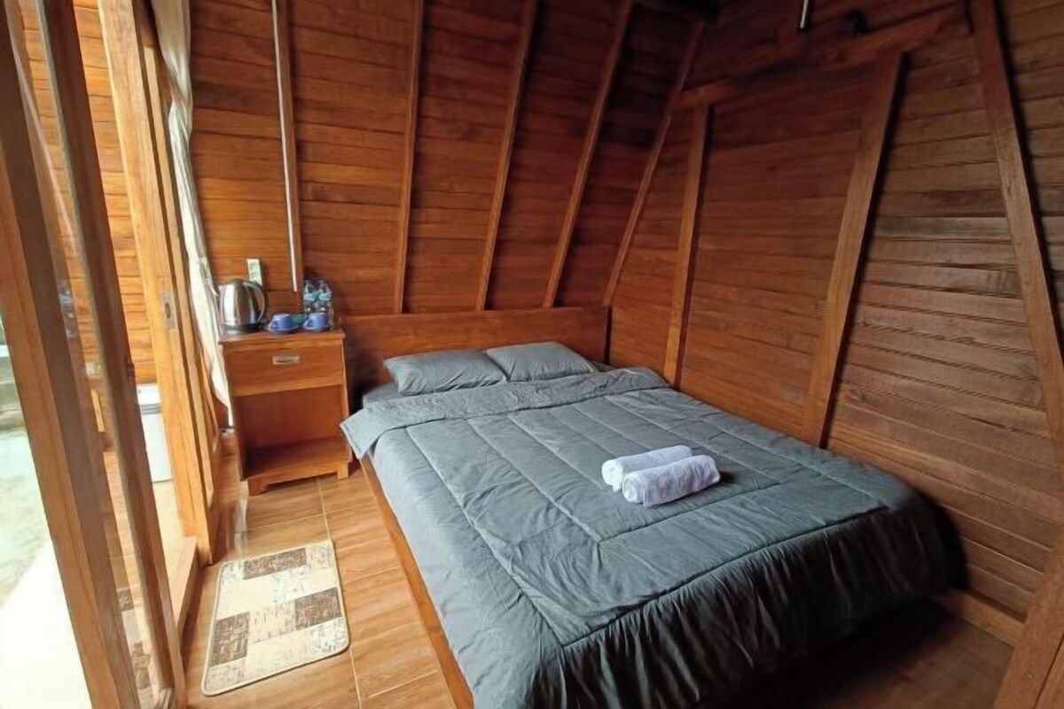 Een kamer met houten vloer, een bed, nachtkastje en een klein tafeltje met waterkoker en kopjes.