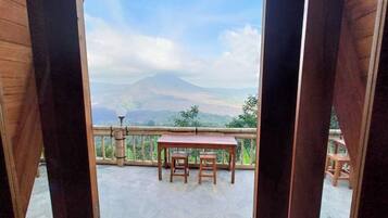 A balcony with a wooden table and chairs, offering a view of a mountain.