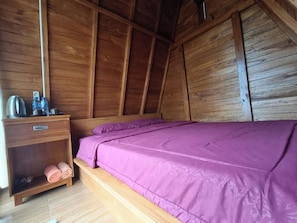 Quarto de madeira com uma cama, uma mesinha de cabeceira e uma prateleira com toalhas.