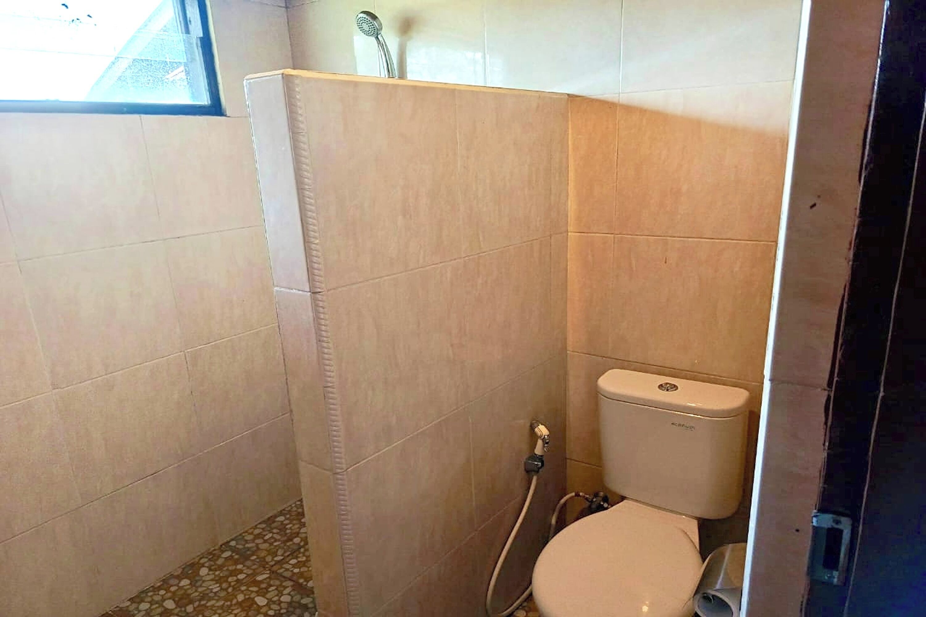 A small, tiled bathroom with a toilet, shower, and a window.