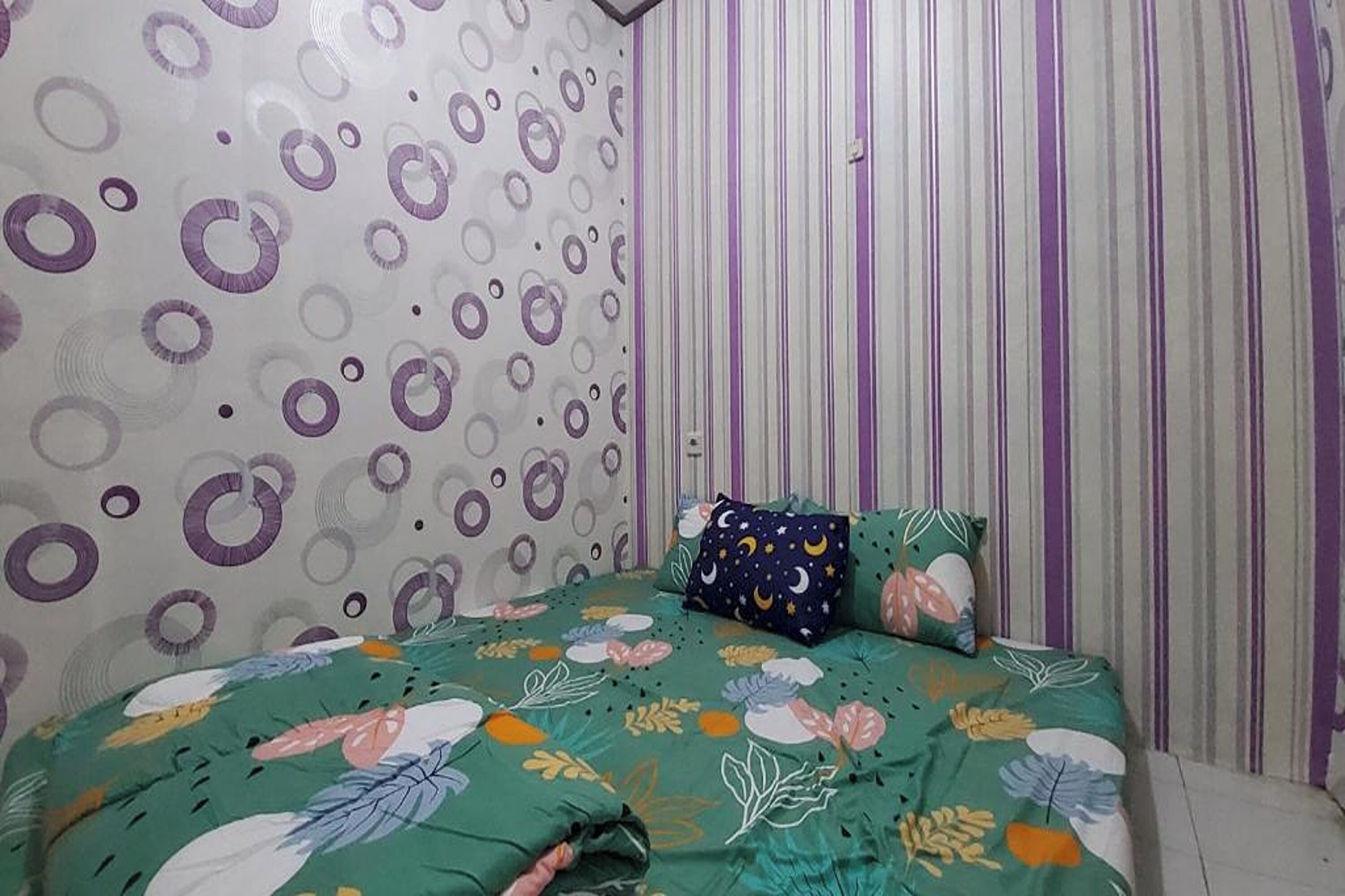 A bedroom with a patterned wall, a striped curtain, and a floral bedspread.