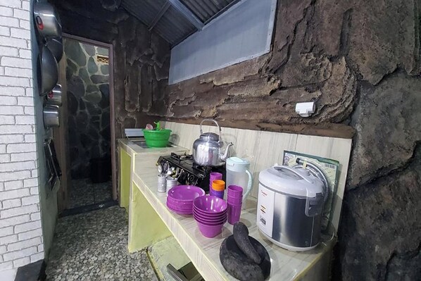 A kitchen with a stone wall, a sink, and various kitchen utensils and appliances.