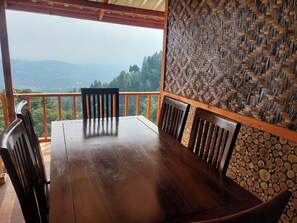 A wooden table with four chairs in a covered outdoor area with a view of the mountains. - Villa Zoya Montana (Megamendung)