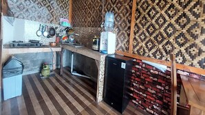 Une cuisine compacte avec un mur décoré d’un motif, une cuisinière à gaz, un distributeur d’eau et un petit réfrigérateur.