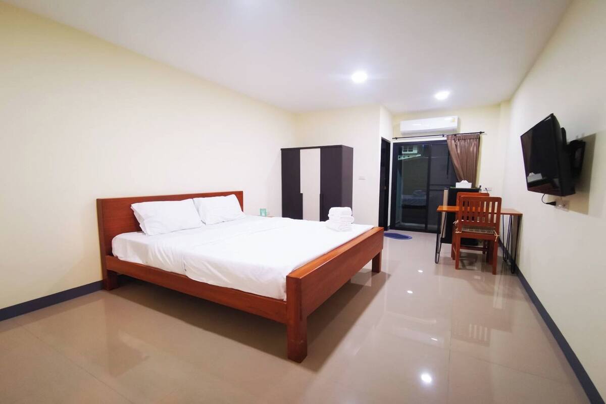 Een hotelkamer met een houten bed, een bureau, een stoel, een televisie en een airconditioner.
