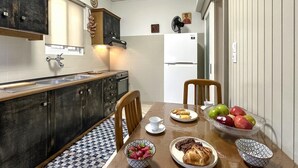 Una cocina compacta con armarios de madera oscura, un lavamanos de acero inoxidable y un refrigerador blanco. Una mesa de comedor con sillas está dispuesta con platos de comida y un tazón de fresas.