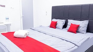 Un lit bien fait, avec une couverture grise et rouge, une serviette blanche et deux oreillers rouges.