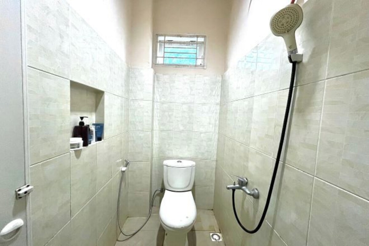 Une petite salle de bain carrelée, équipée de toilettes, d’une douche et d’une fenêtre.