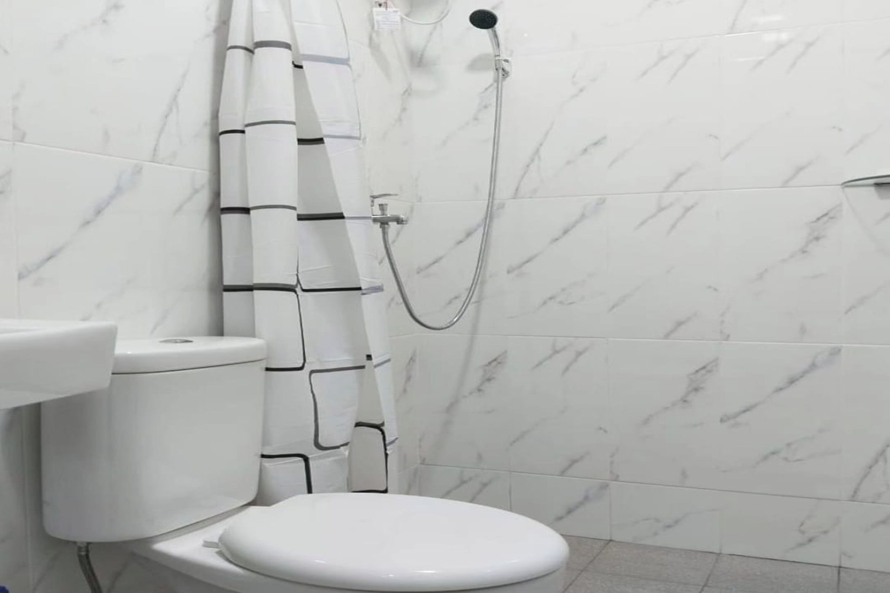 A bathroom with a toilet, a shower, and a marble-tiled wall.