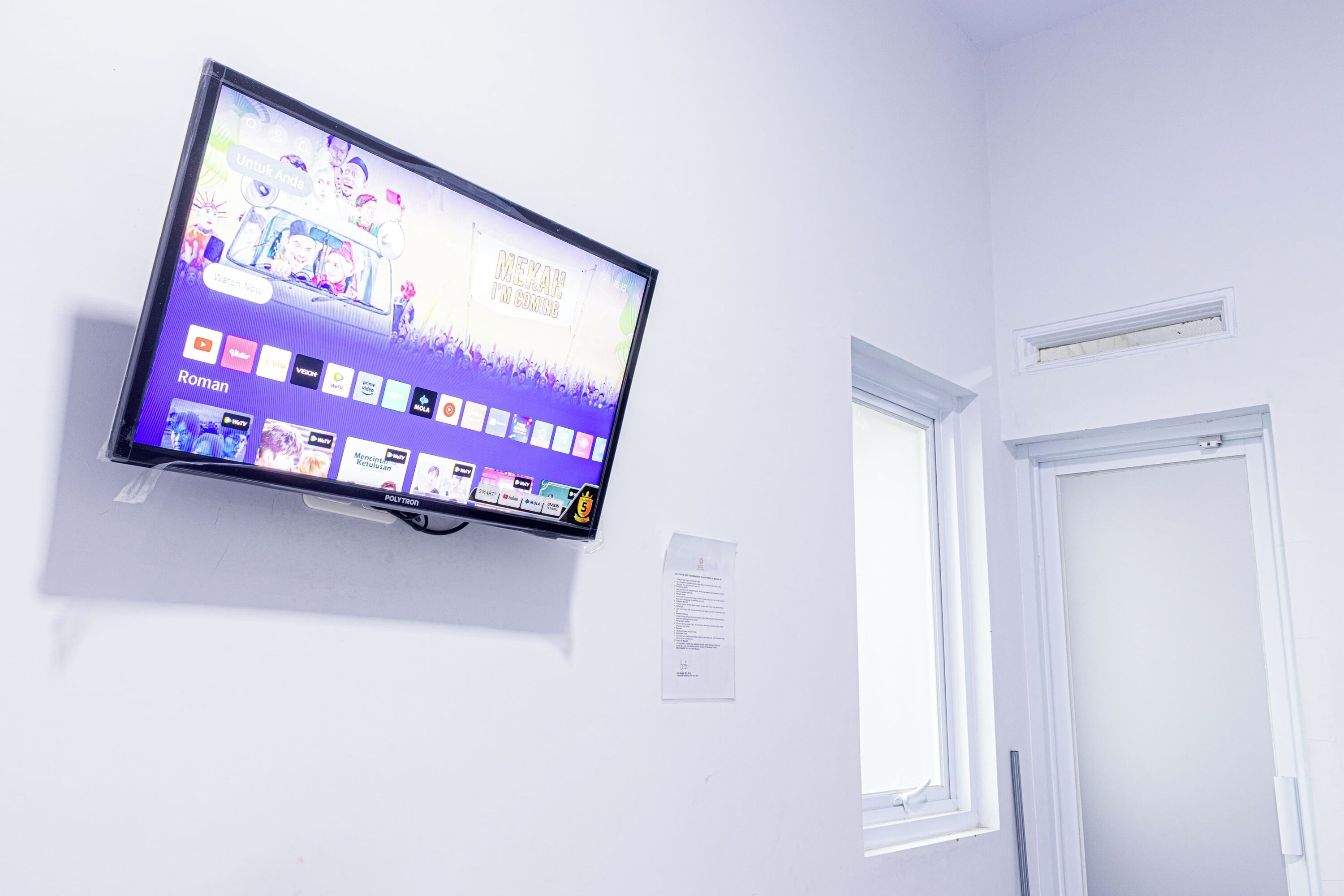 Televisão de tela plana fixada em uma parede branca, exibindo um videoclipe com diversos ícones de aplicativos abaixo.
