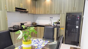 Une cuisine moderne avec des meubles en bois, un réfrigérateur noir, une cuisinière et une table à manger avec un plateau en verre.