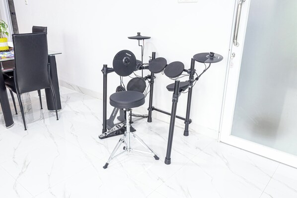 A drum set in a room with a white tiled floor and a black chair. - Inara Guesthouse & Villa (Tasikmalaya)