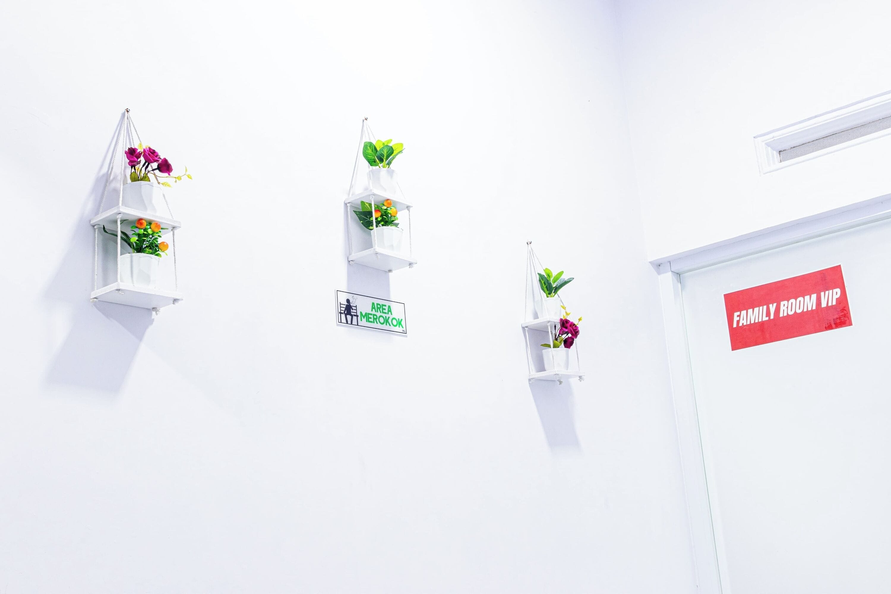 Drie witte wandplanters met bloemen en een bordje met de tekst 'AREA MEROKOK'.