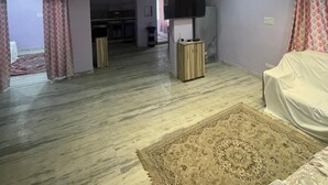A spacious living room with a high ceiling, a flat-screen TV mounted on the wall, and a large patterned rug on the floor. - duplexhotel (Hyderabad)