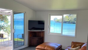 Una sala moderna con un amplio ventanal que da a un cuerpo de agua, un televisor de pantalla plana, un sofá de cuero y una mesa de centro de madera.