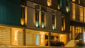 Un hôtel à plusieurs étages doté de balcons, de climatiseurs et d’un parking pour voitures et motos.