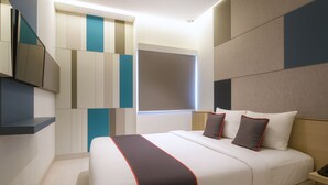 Une chambre d’hôtel moderne dotée d’un grand lit, d’un téléviseur à écran plat fixé au mur et d’une fenêtre avec des stores.