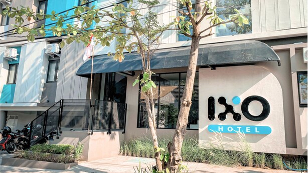 Un hôtel moderne avec une enseigne indiquant « IXO HOTEL » et un arbre au premier plan.