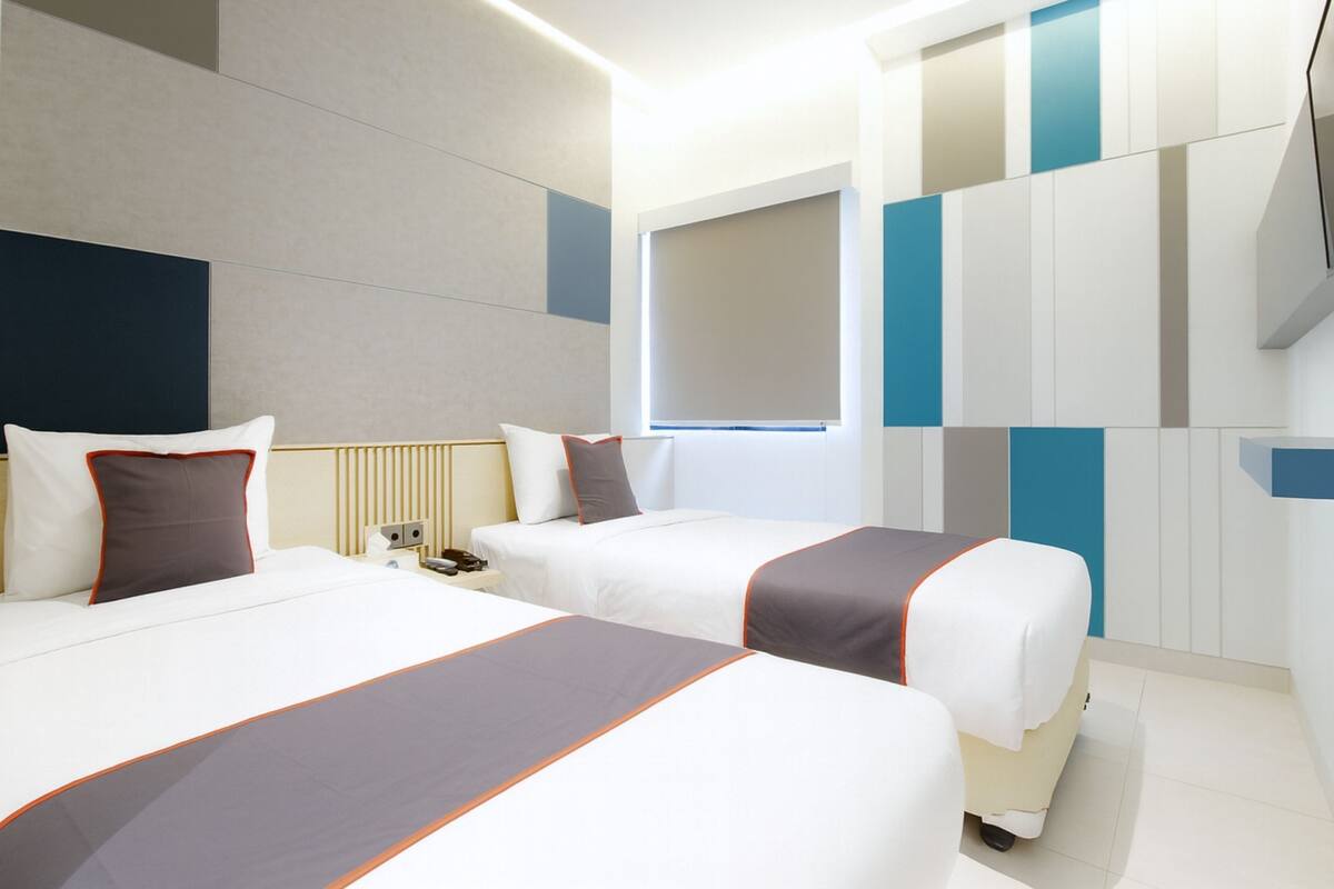 A hotel room with two beds, a large window, and a modern design.