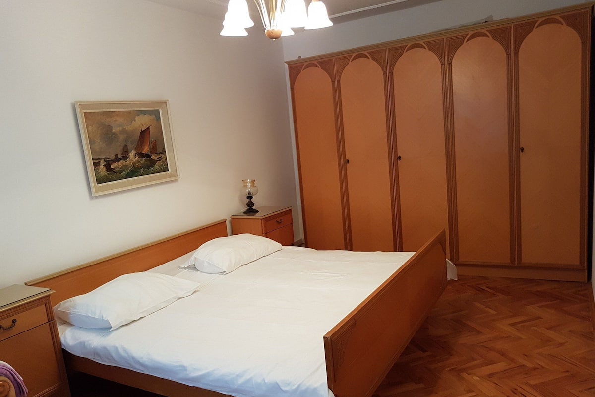 Une chambre à coucher avec un lit en bois, une table de chevet, une lampe, une armoire et un tableau au mur.